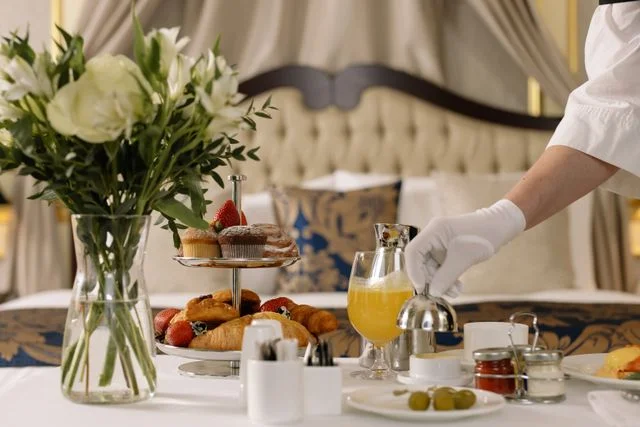 Gloved hotel staff serving in-room breakfast with fresh pastries and orange juice, luxury hospitality service
