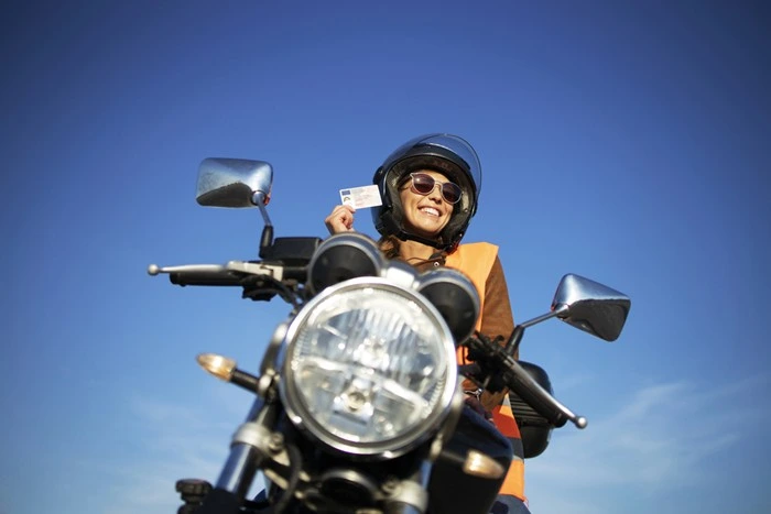 Motorcyclist in high-visibility vest holding driving license by her bike