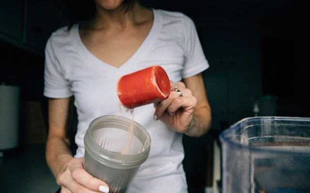 Best collagen and protein drinks for women, pouring protein powder into a shaker cup