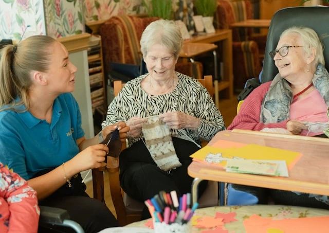 Caregiver joining elderly residents in a knitting activity at a nursing home