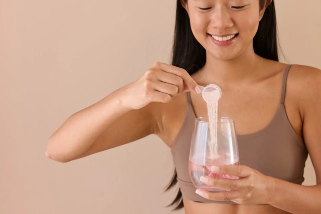 Woman scooping collagen powder into a glass of water for a daily protein drink