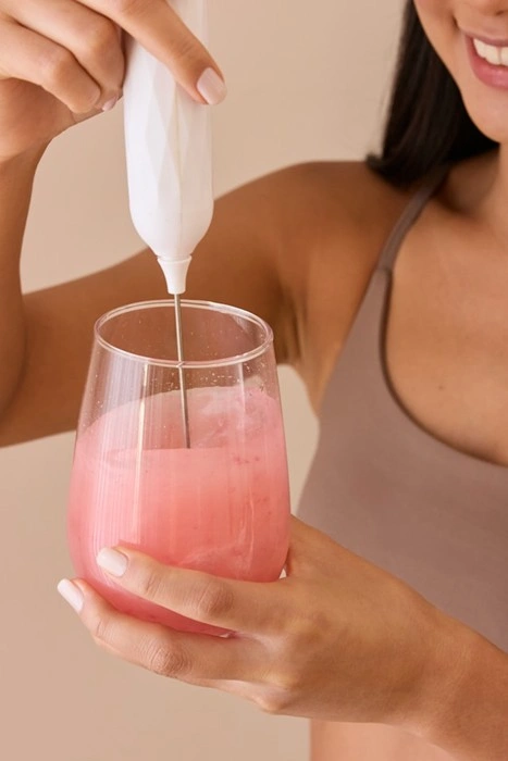 Woman mixing a pink collagen protein drink with a portable frother