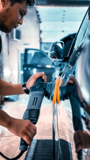 Technician polishing a repaired car door panel with an orbital buffer at a BMW body shop in Dubai