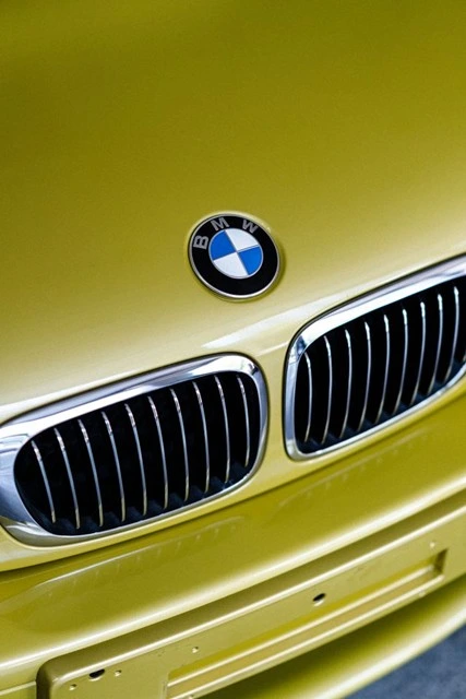 Close-up of a BMW badge and kidney grille on a metallic yellow hood with a glossy factory paint finish