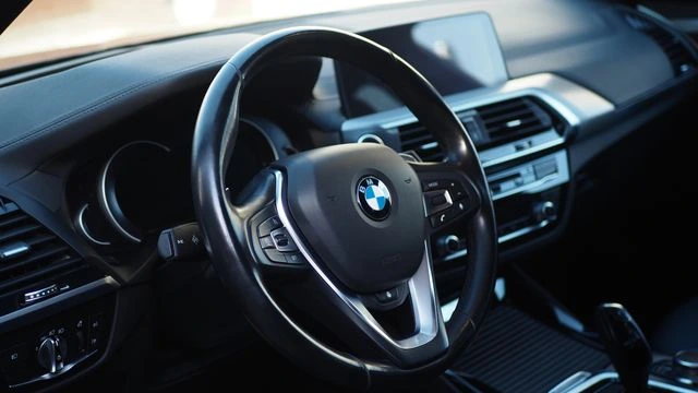 Interior of a BMW SUV with a leather steering wheel, a black dashboard, and a central infotainment screen in warm afternoon light