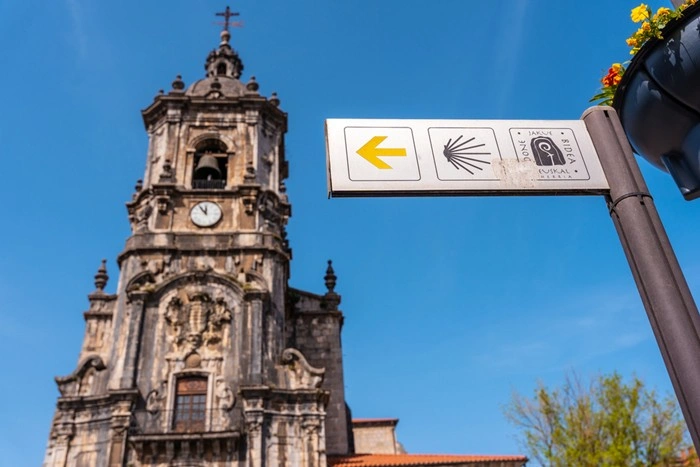 Camino trail sign with scallop shell near a historic church tower in Spain