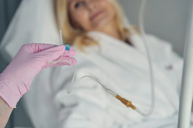 Nurse in pink gloves preparing an implantable port injury patient's catheter line in a hospital bed