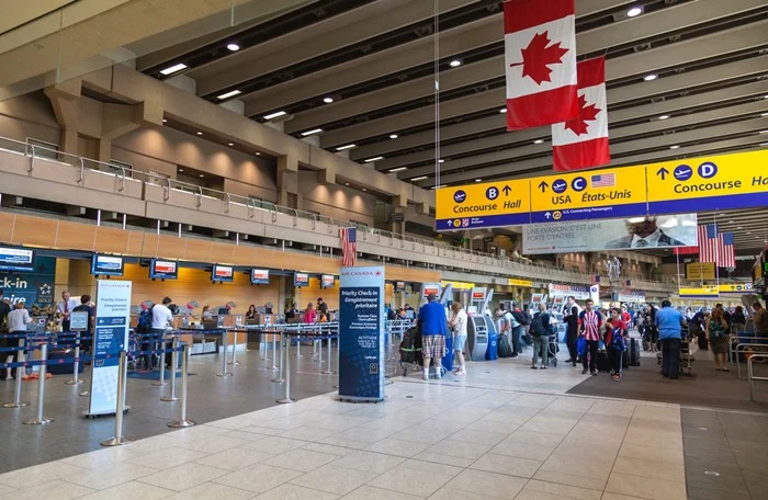 Canadian flags hanging over a busy airport terminal in Canada, with travelers waiting near the Air Canada check-in counters before their flight