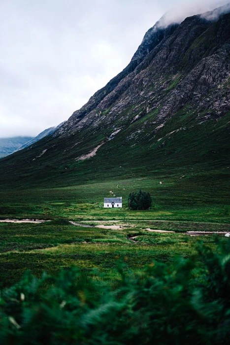 Isolated white cottage in a green valley beneath misty mountains, capturing the essence of countryside travel in Scotland