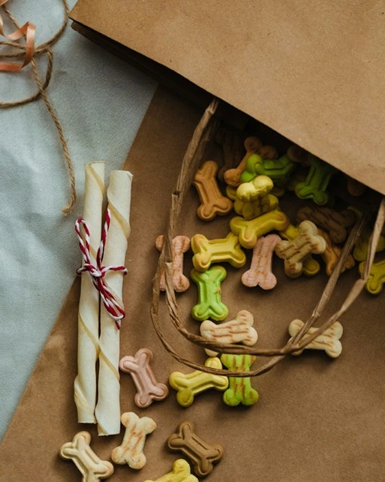 Bone-shaped dog snacks and chew sticks spilling out of a paper bag