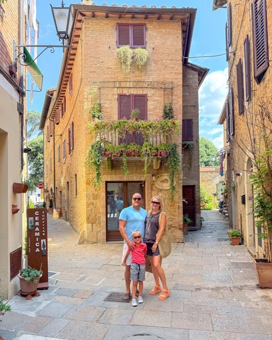 Family traveling in Tuscany, standing in a narrow stone alley beside a flower-covered villa