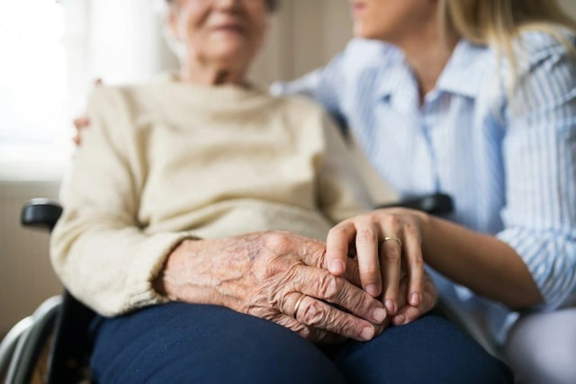 Family member visiting and holding hands with an elderly relative in a wheelchair