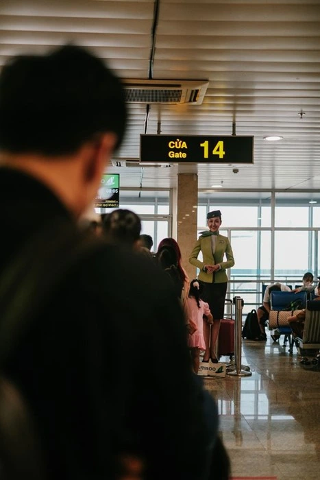 Travelers queuing at Gate 14 in a Vietnam airport as a flight attendant in a green uniform greets passengers before boarding