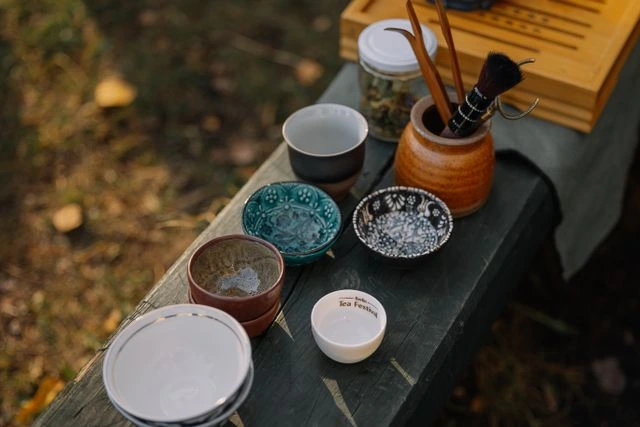How to choose a travel tea set with an assortment of ceramic teacups and a gongfu brewing tool holder arranged outdoors on a wooden bench