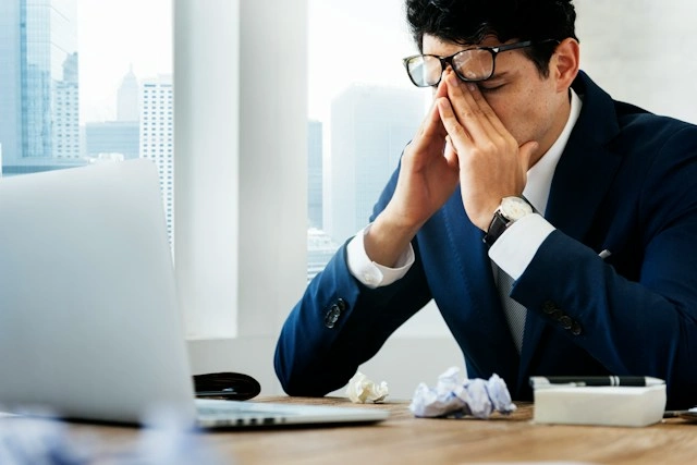 Stressed businessman covering his face at his desk, illustrating how to recover from a setback at work