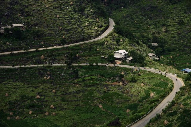 Winding mountain road through green terraced hillsides in northern Vietnam, dotted with small houses and haystacks, where travel signal can be patchy