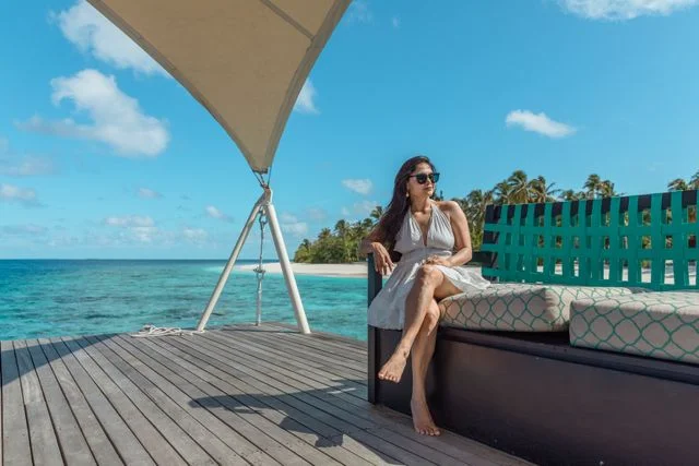 Woman seated on private overwater deck lounge with turquoise sea and palm trees in the background