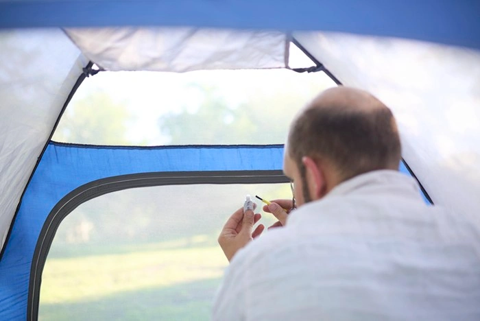 Camper applying emergency tape for camping to a torn tent mesh panel