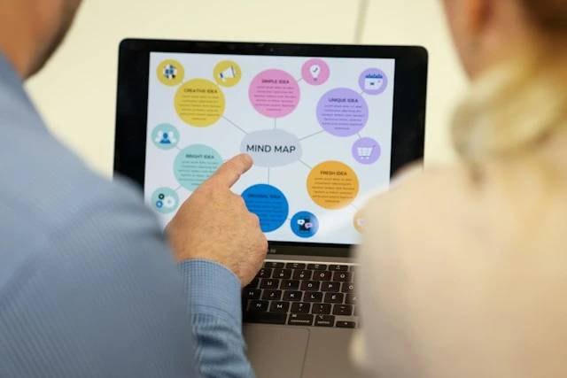 Two people reviewing a colorful mind map on a laptop screen, exploring ideas to reshape their perspective