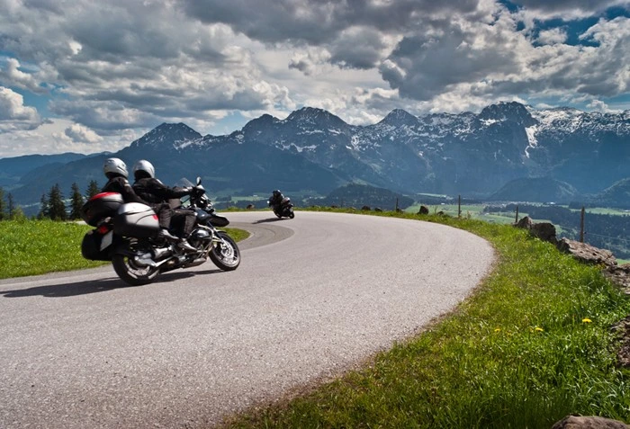 Motorcyclists riding a winding alpine road with mountain views