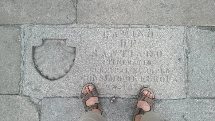 Pilgrim's feet standing on the Camino de Santiago plaque marking journey's end