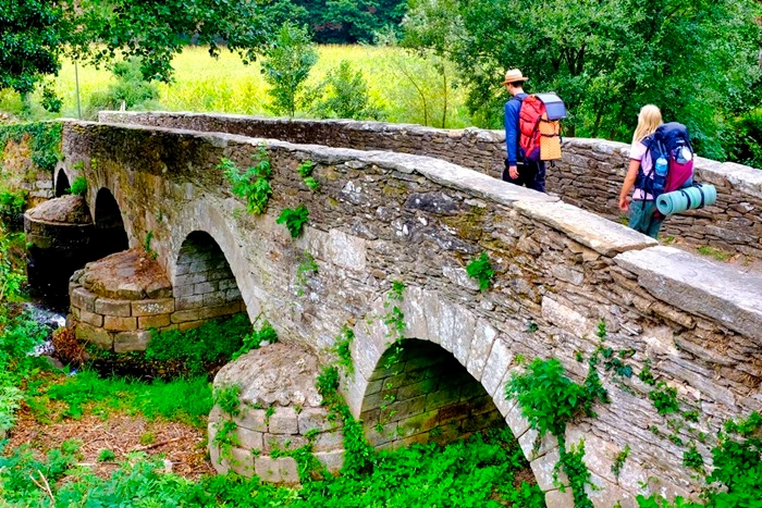Pilgrims with backpacks crossing a stone bridge on the Camino de Santiago route