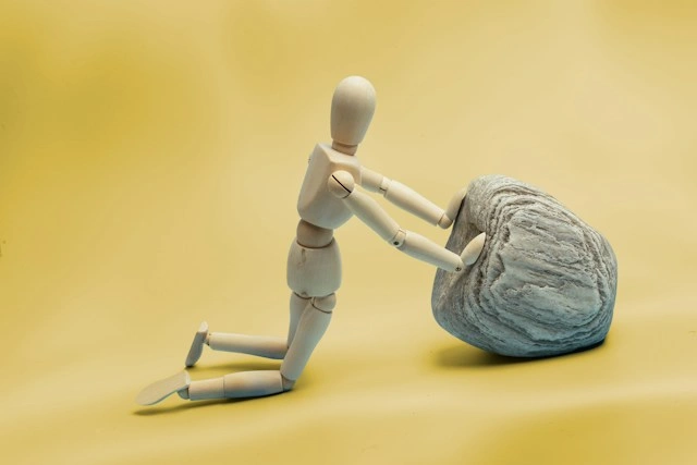 Wooden figure pushing a heavy stone uphill, representing resilience and effort during a setback