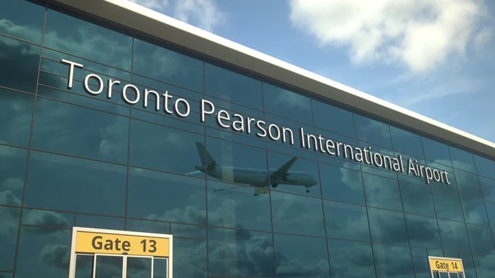 Glass facade of Toronto Pearson International Airport in Canada, reflecting a departing flight above the signs for Gates 13 and 14