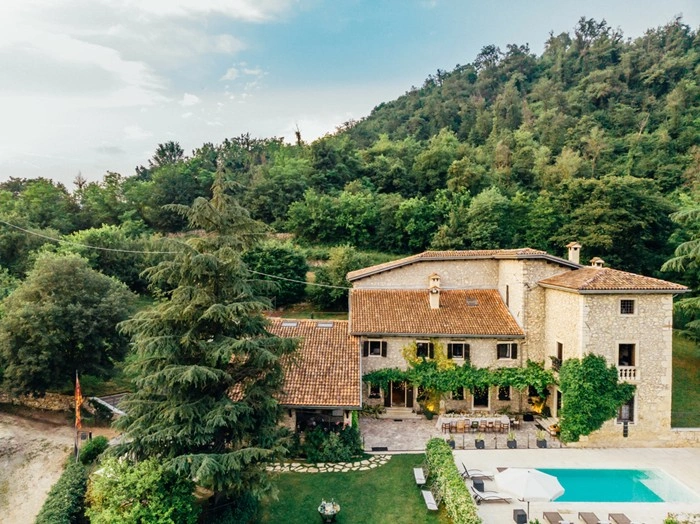 Stone villa with a pool in Tuscany, set against a wooded hillside with a shaded terrace