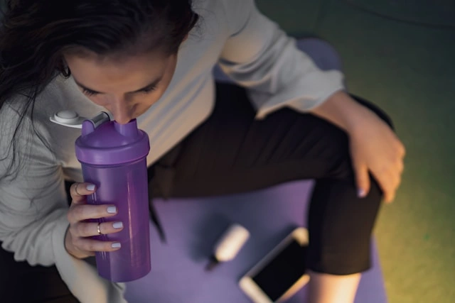 Woman drinking a protein shake from a tumbler after a workout
