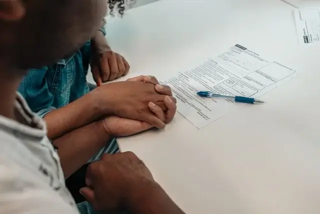 Two people holding hands at a table beside a legal form and a blue pen while reviewing post-divorce parental responsibility in Florida