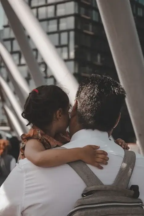 A father carrying his young daughter in a city setting as she hugs him, reflecting shared parental responsibility in Florida