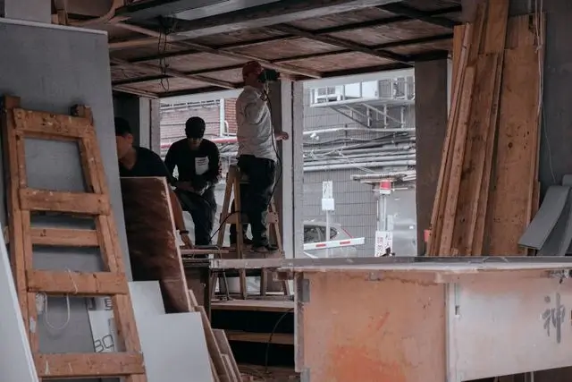 Construction crew handling plywood and ladders while a team member stays connected by mobile phone