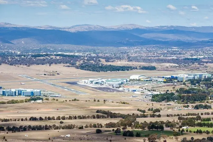Aerial view of Canberra Airport with its runway and terminal, set against rolling hills, the first stop for many visitors to the city