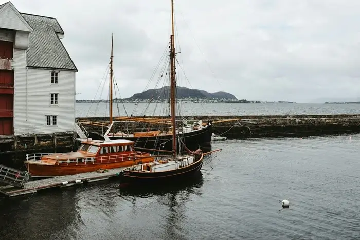 Traditional wooden boats docked at a stone harbor wall with misty islands beyond, a charming coastal stop on a Nordic trip