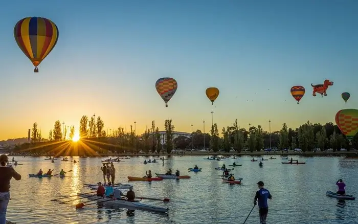 Hot air balloons drift over Lake Burley Griffin at sunrise as kayakers and paddleboarders enjoy the water, a magical Canberra moment for first-time visitors