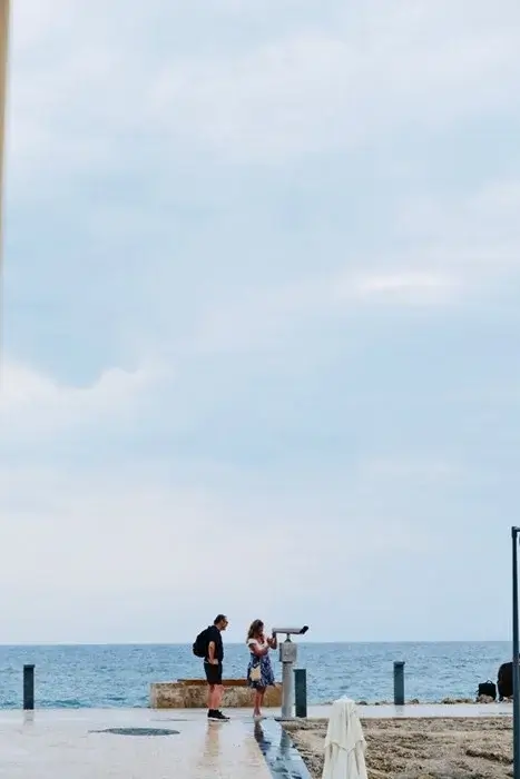 Couple standing by a seaside viewing binocular on an overcast day, a slow travel moment during an international first meeting