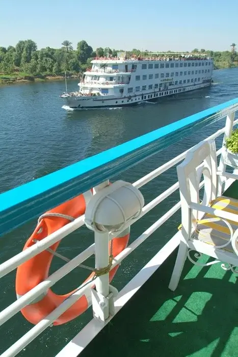 View from a cruise boat deck with an orange life ring as another river ship sails past palm trees on the Nile