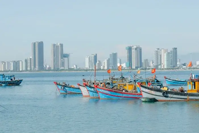 Traditional blue and red fishing boats on calm water with high-rise hotels along the Da Nang coastline in Vietnam