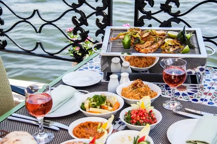 Al fresco dining on a Nile boat with a tabletop grill, rice dishes, fresh salads, and glasses of wine by the river