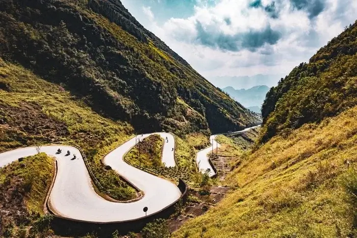 Riders on a curving mountain pass through green valleys in Ha Giang, one of the most scenic road trips in Vietnam