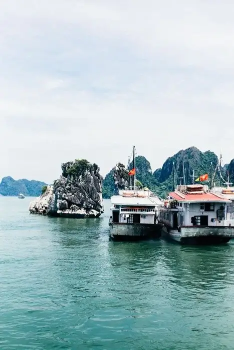 Traditional cruise boats with Vietnamese flags anchored near limestone rocks in Ha Long Bay, northern Vietnam