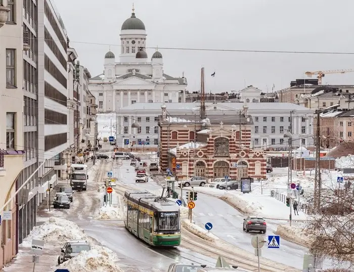Snow-covered streets of Helsinki with a city tram, the red-brick Old Market Hall and the white cathedral dome rising behind