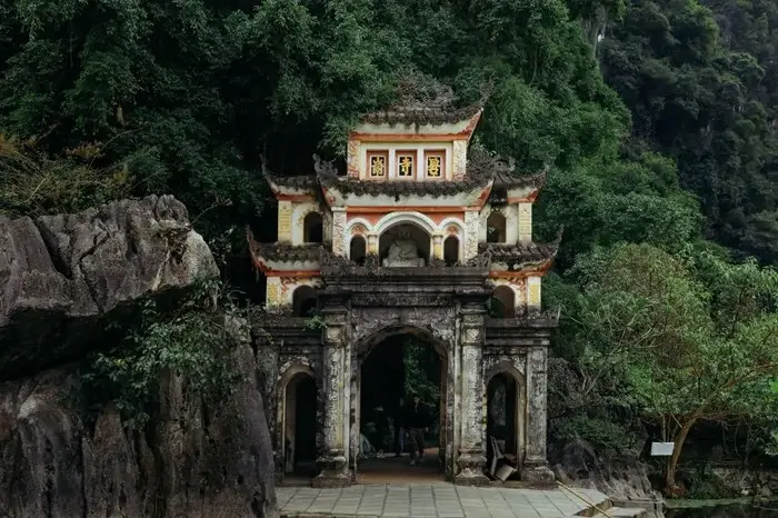 Ancient stone gate of Bich Dong Pagoda set against lush limestone cliffs in Ninh Binh, a peaceful place to visit in Vietnam