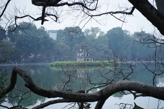 Turtle Tower on a small island in Hoan Kiem Lake, framed by bare tree branches in Hanoi, a historic place to visit in Vietnam