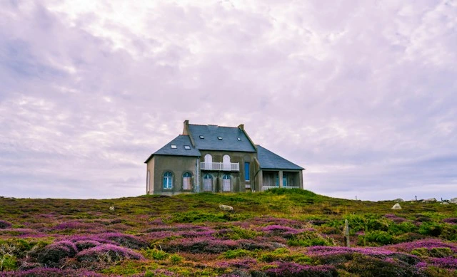 Isolated stone home on a heather-covered hilltop under a cloudy sky, far from quick help after a fire or flood
