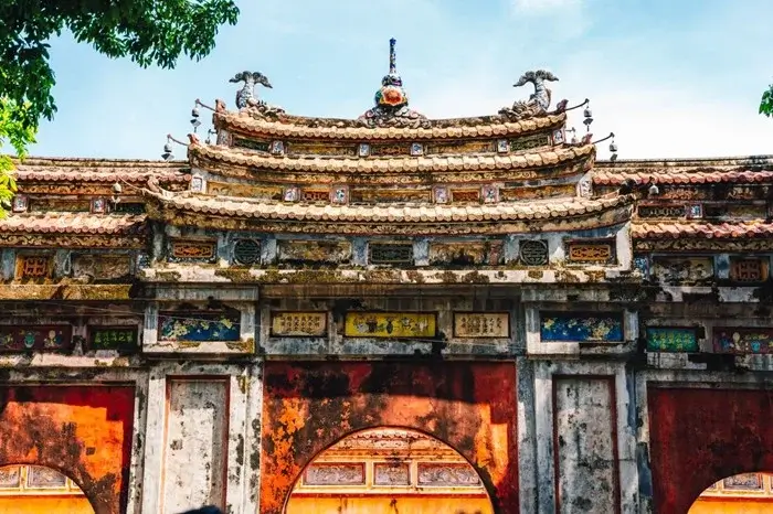 Faded red archways and decorative rooftop details of an ancient gate at the Imperial City in Hue, Vietnam