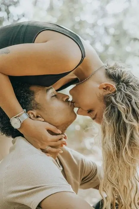 Woman leaning down to kiss her partner under soft green foliage, the payoff of a cross-border relationship
