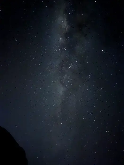 Milky Way stretching across a clear night sky above a dark rock silhouette while climbing Kilimanjaro