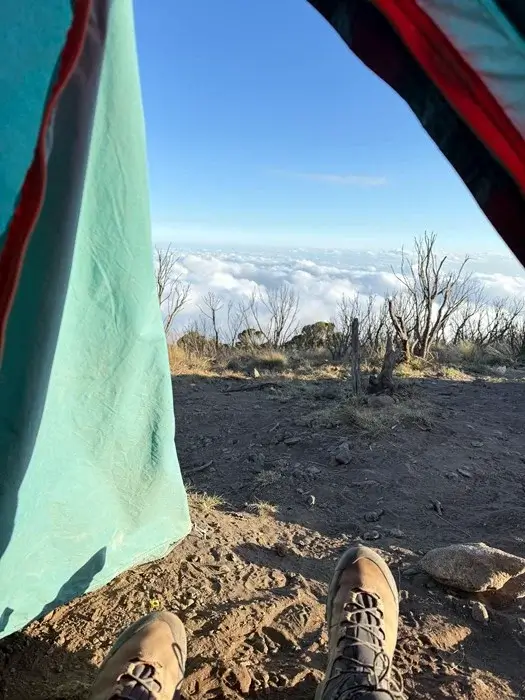 View from a tent door of a sea of clouds at sunrise while climbing Kilimanjaro, with hiking boots in the foreground